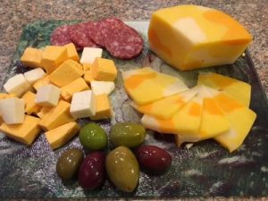 Cheddar cheese and curds, salami and olives on a plate